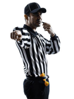 Picture of a referee holding a whistle to his mouth while pointing directly toward the person viewing the picture