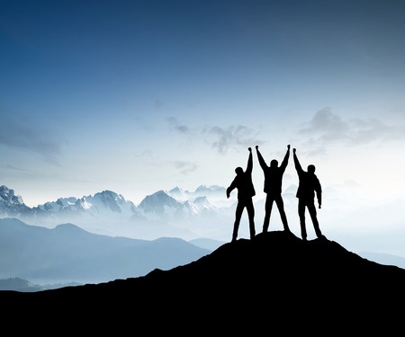 Three people standing on top of a mountain with their hands held high together